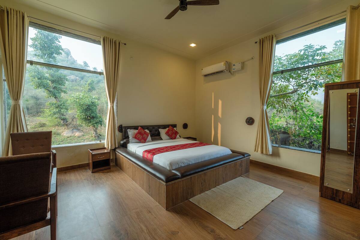 A bedroom with a wooden bed, a nightstand, a chair, and a large window with curtains.