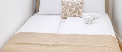 A neatly made bed with a beige bedspread, white pillows, and a patterned pillow.
