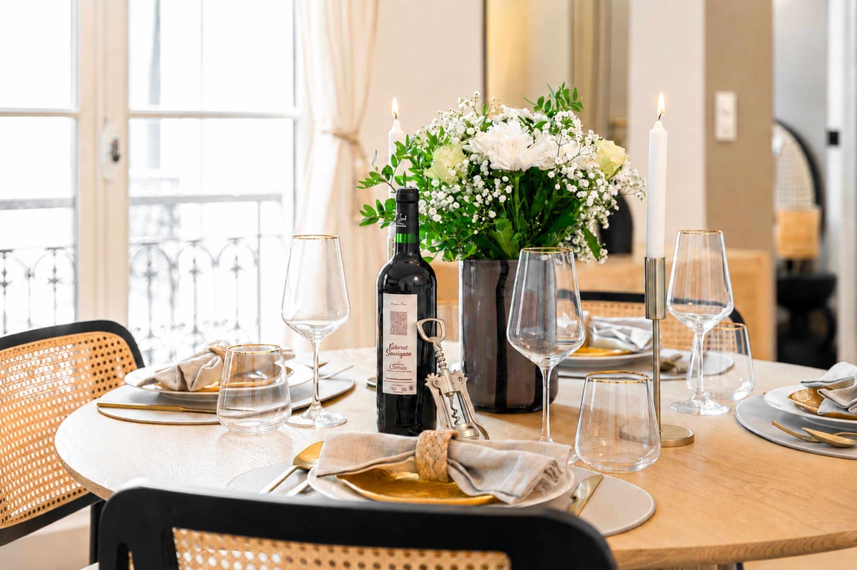 A dining table set with wine glasses, a bottle of wine, a vase with flowers, and a candle.