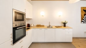 Une cuisine moderne avec des meubles blancs, un four encastré, un micro-ondes, un évier et un plan de travail sur lequel se trouvent une bouilloire et un panier.
