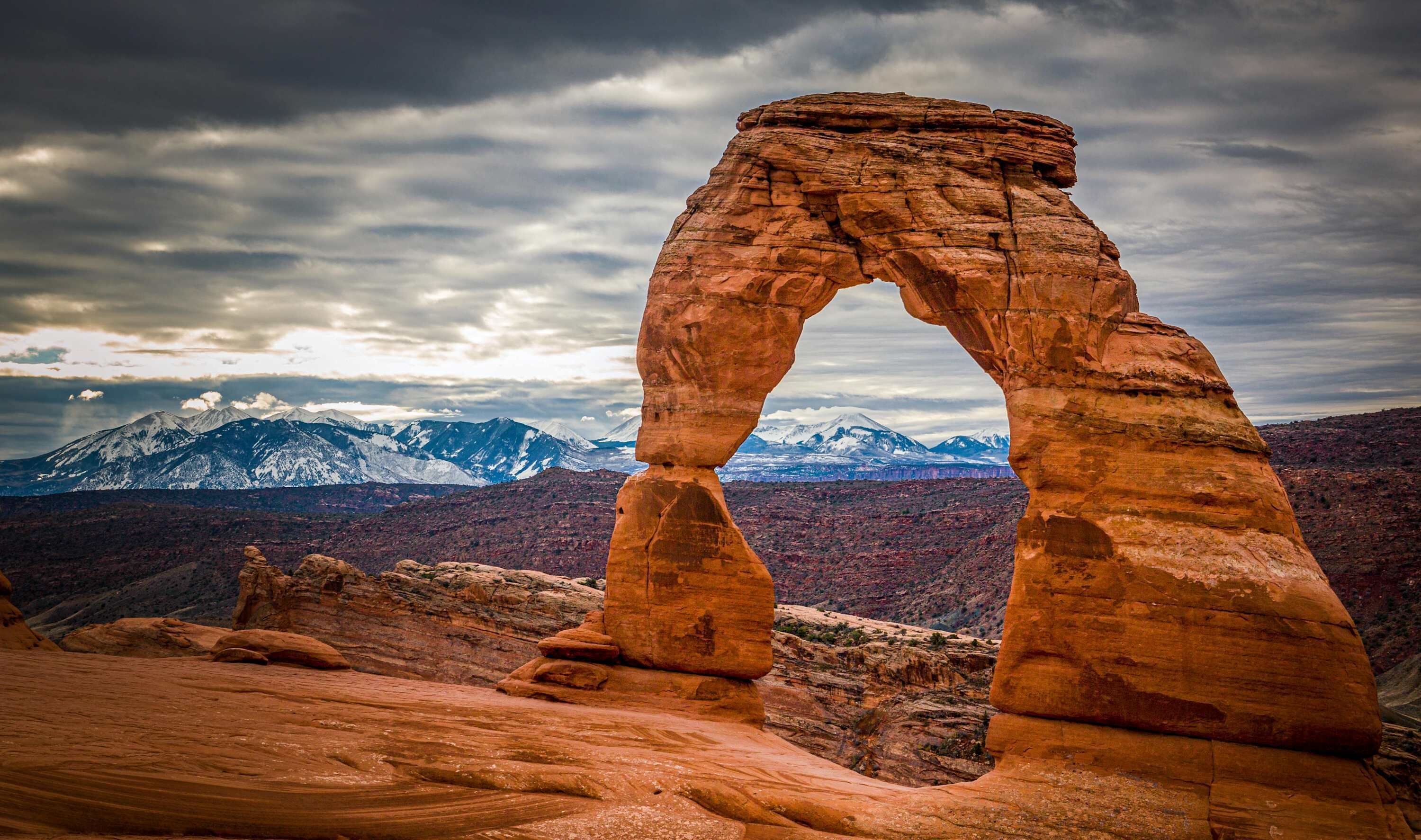 A natural rock arch formation with a mountainous backdrop.