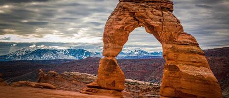 A natural rock arch formation with a mountainous backdrop.
