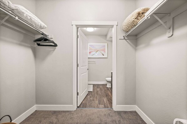 A narrow hallway with a door leading to a bathroom. There are hooks on the walls for hanging items, and a carpeted floor.