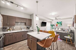 A modern kitchen with dark wood cabinets, a white countertop, and a dining area with a table and chairs. - Downtown SLC - Hot Tub - Gym - Free Parking (Salt Lake City)