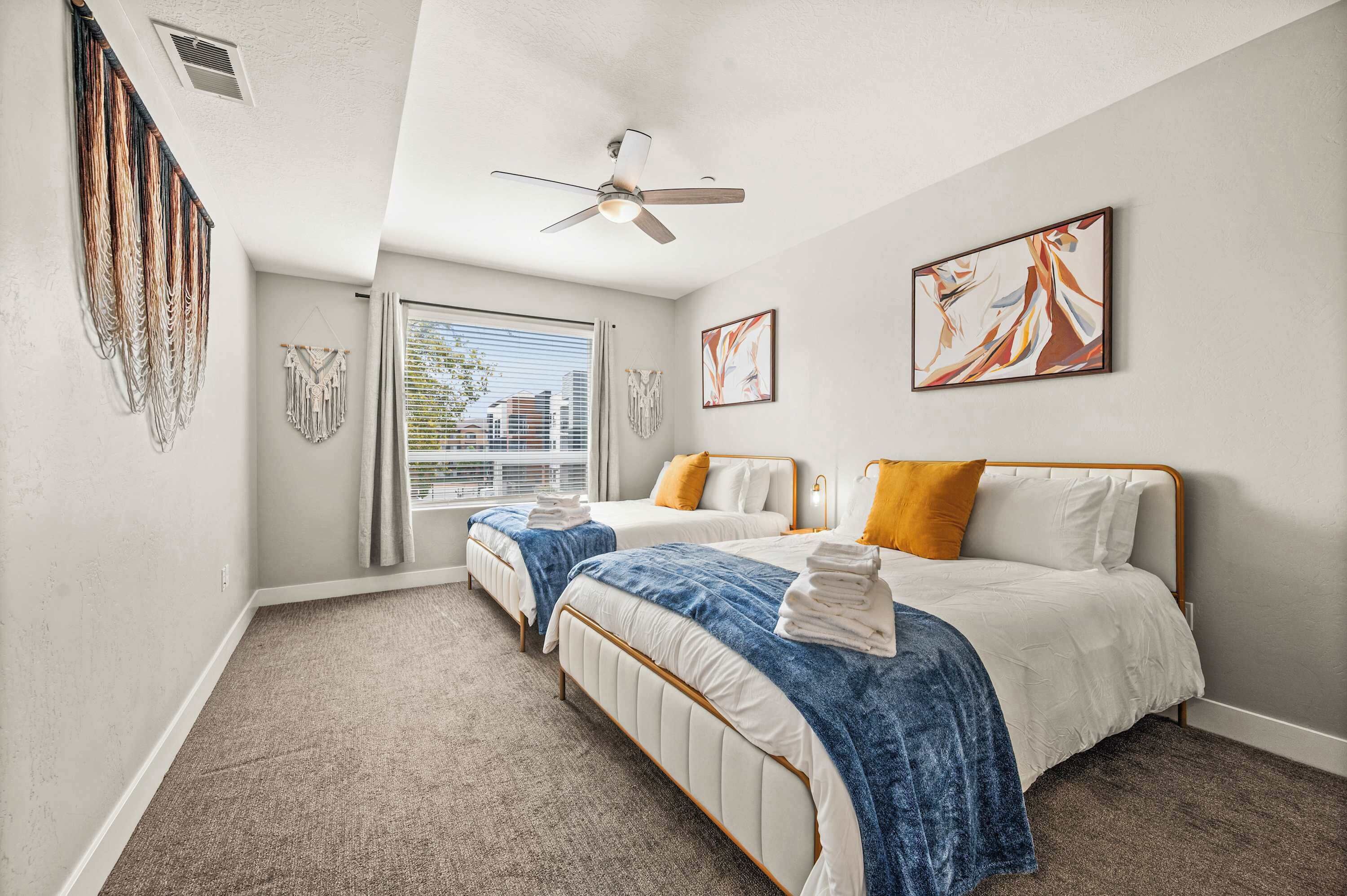 A bedroom with two beds, a ceiling fan, and artwork on the walls.