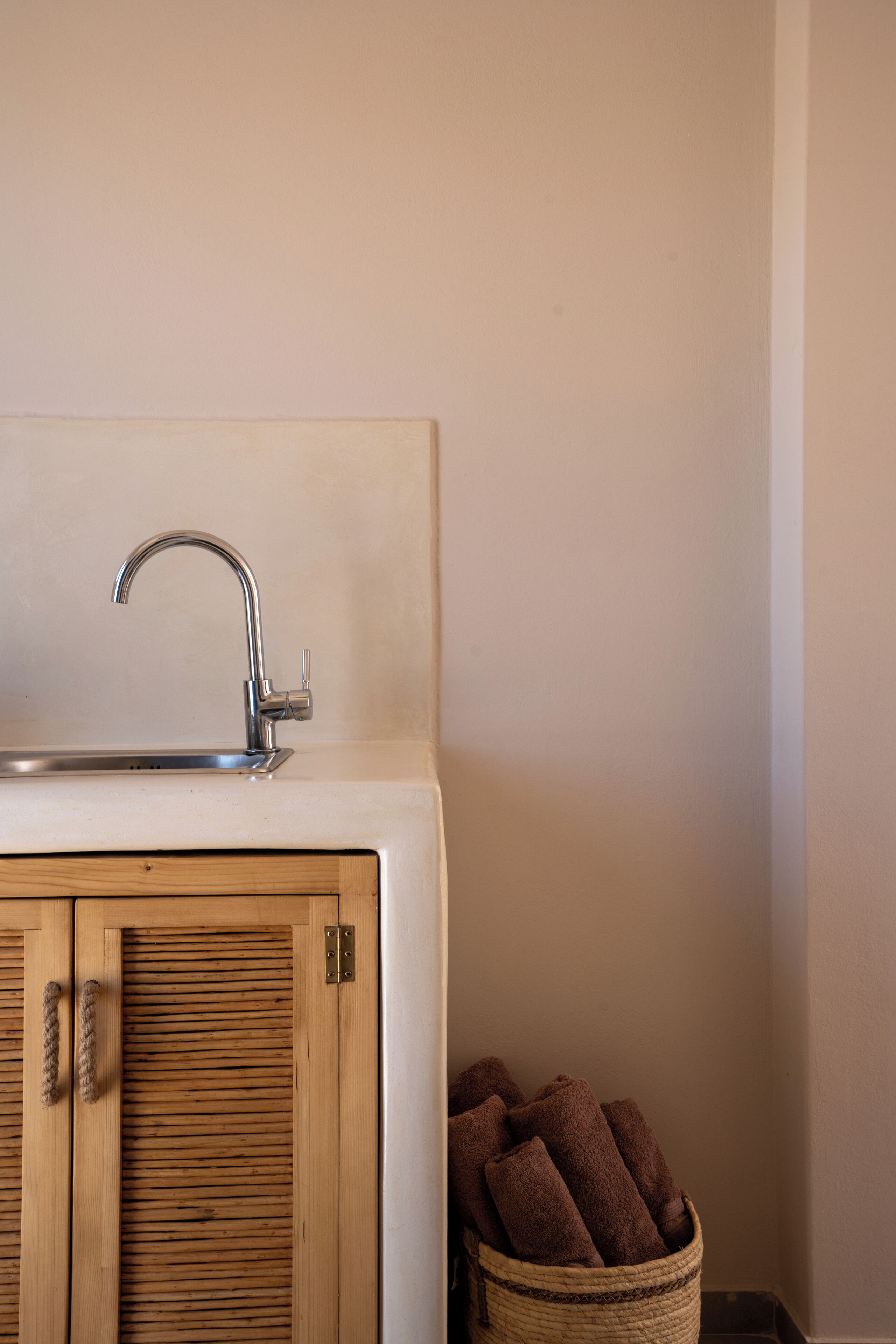 Un baño con un mueble de madera, un lavabo blanco con un grifo moderno y una cesta de mimbre con toallas.