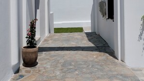 A narrow stone-paved corridor with white walls and an archway leading to a green lawn. - Cycladic Charm (Naousa)