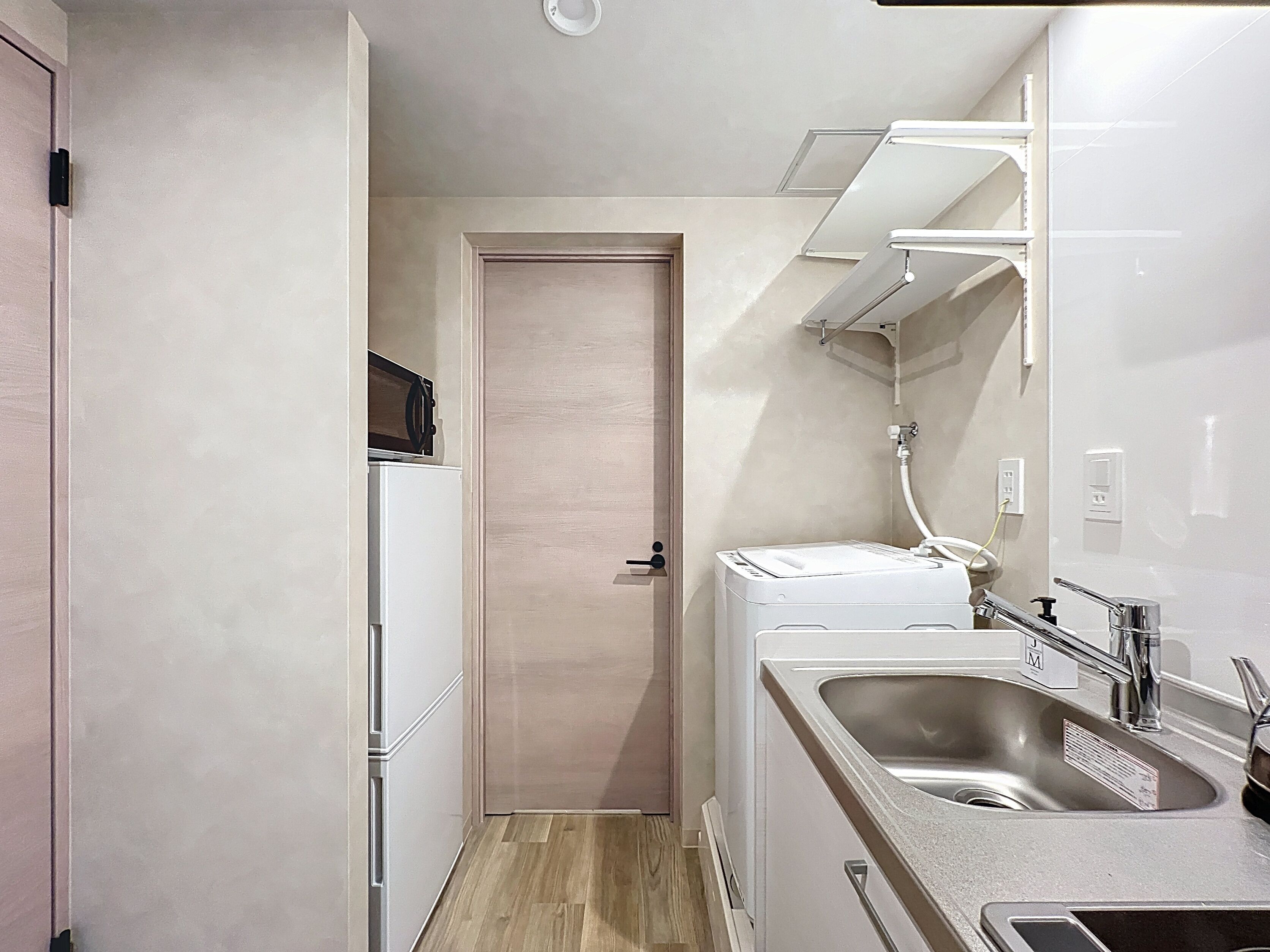 A compact kitchen with a built-in washing machine, a sink, and a door leading to another room.