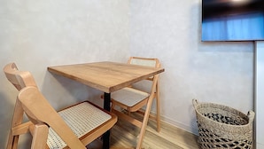 A small room with a wooden table and chairs, a woven basket, and a mounted television. - Viento Ikebukuro (Tokyo)