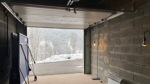 A garage with a concrete wall, a white ceiling, and a door leading outside. There is a whiteboard on a stand, a heater, and a light fixture on the wall. - Chalet on the edge of town, close to the Balme cable car (La Clusaz)