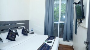 Quarto de hotel com cama, travesseiros, televisão e janela com cortinas.
