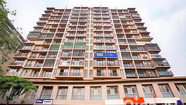 Um edifício residencial de vários andares com varandas, uma loja visível no térreo e um céu claro.