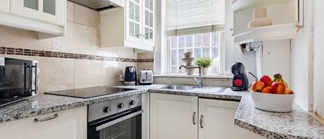 A kitchen with white cabinets, a granite countertop, a stove, a sink, and a window with blinds.