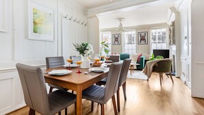 Ein Essbereich mit einem Holztisch, gedeckt für vier Personen, umgeben von Stühlen. Eine Kristallleuchter hängt von der Decke, und an den Wänden befinden sich gerahmte Kunstwerke.