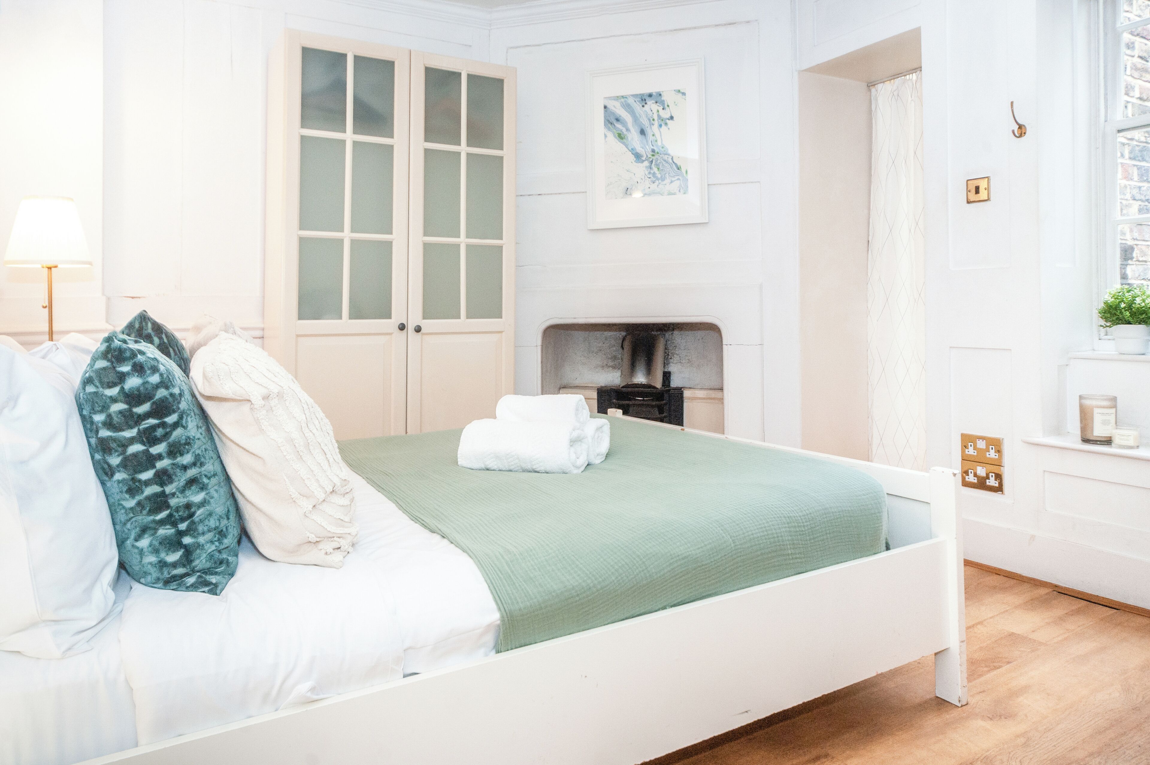 A bedroom with a bed, a nightstand, a fireplace, and a window with curtains.