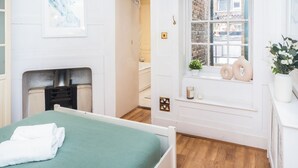 Ein Schlafzimmer mit Bett, Kamin, Fenster mit Blick auf die Straße und einer Regal mit Dekoration.
