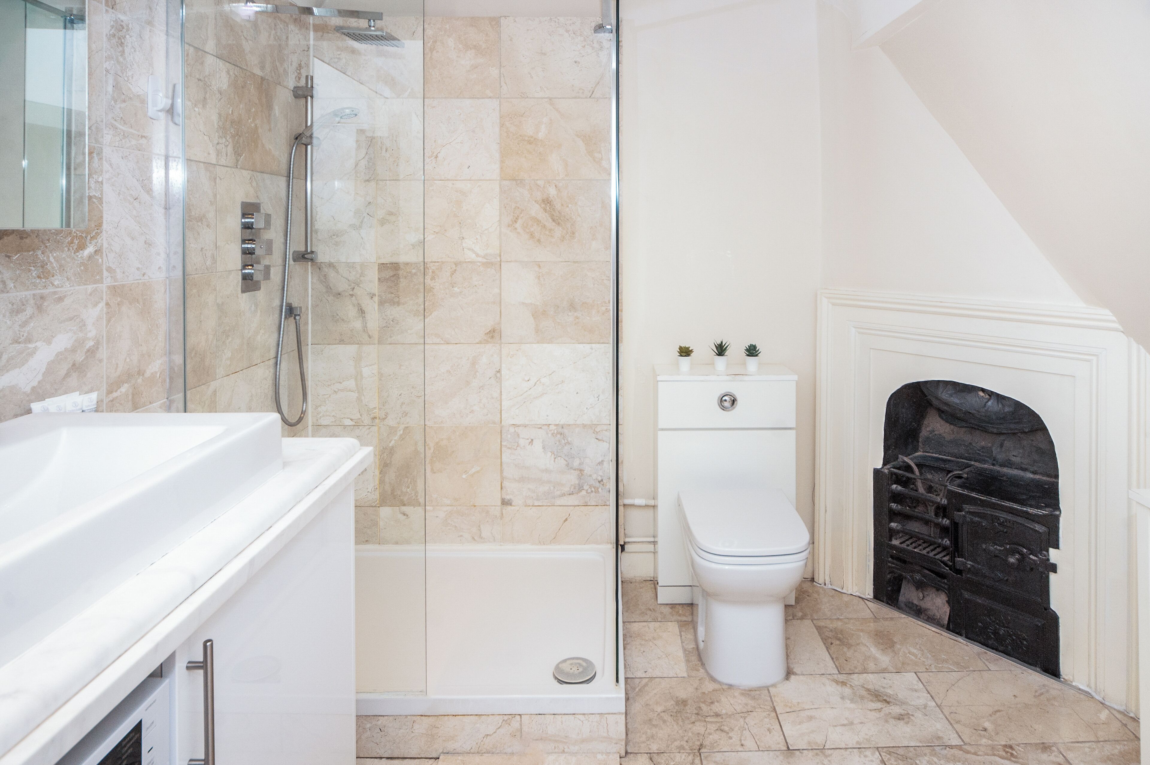 A modern bathroom with a glass-enclosed shower, a white bathtub, a toilet, and a fireplace.