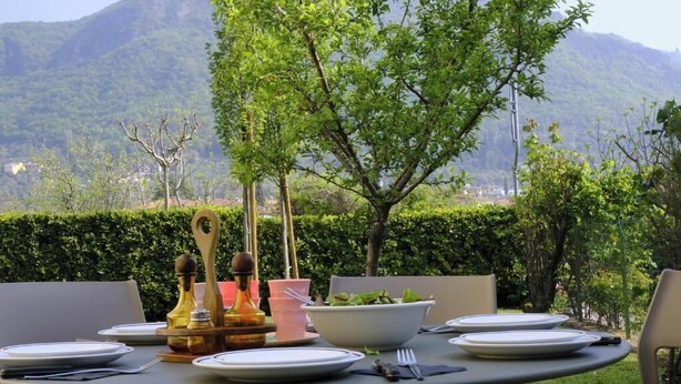 An outdoor dining table set with plates, cutlery, and a bowl of salad, surrounded by chairs, with a mountain backdrop. - Charming villa with private garden and AC in Salo', few steps away from the lake (Salò)