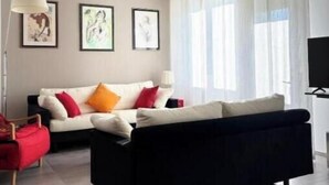 A modern living room with a black sofa, a red chair, a white sofa with colorful cushions, a ceiling fan, and framed artwork on the wall. - Charming villa with private garden and AC in Salo', few steps away from the lake (Salò)
