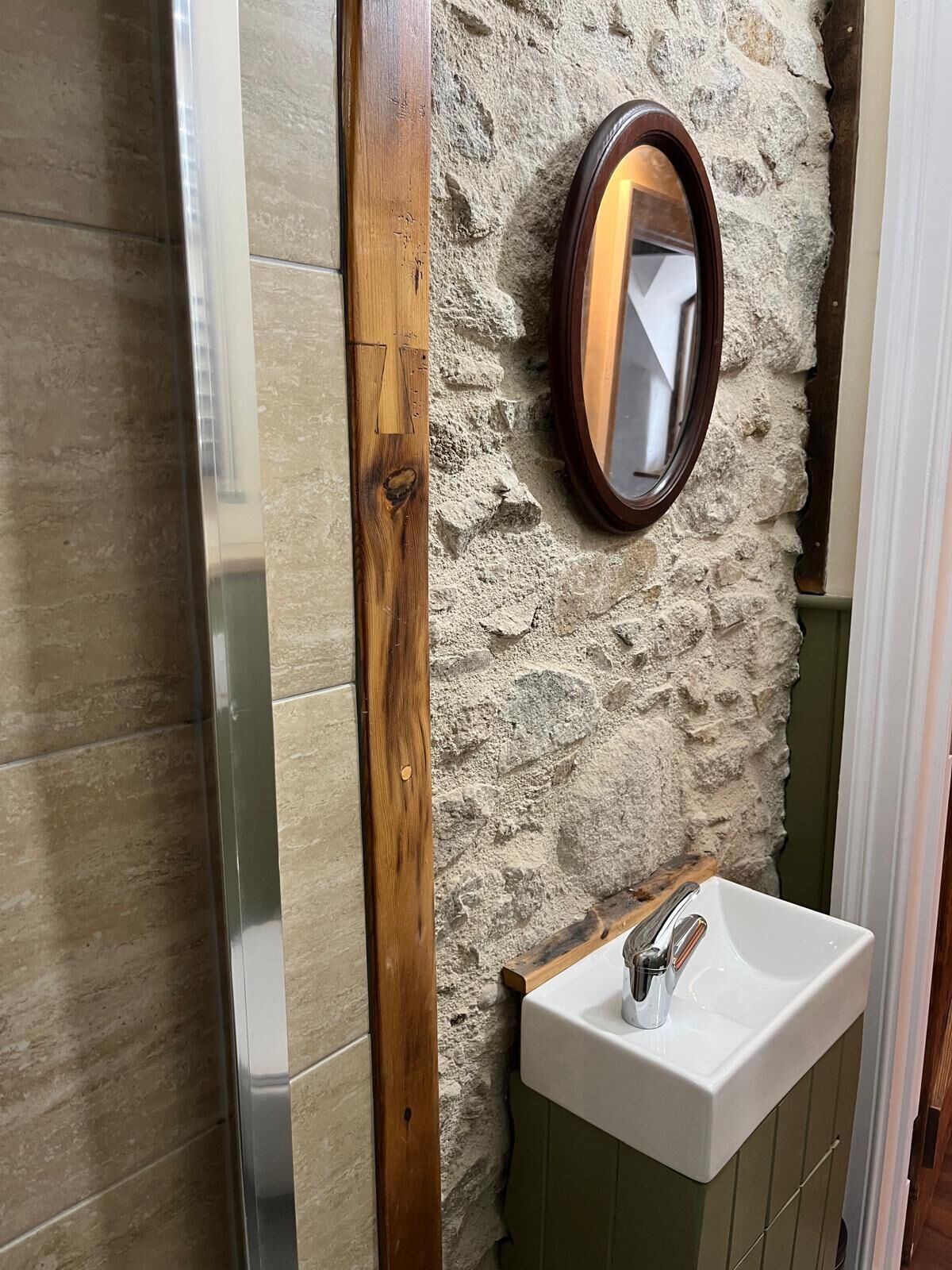 Un baño con pared de piedra, marco de madera, espejo y lavabo.