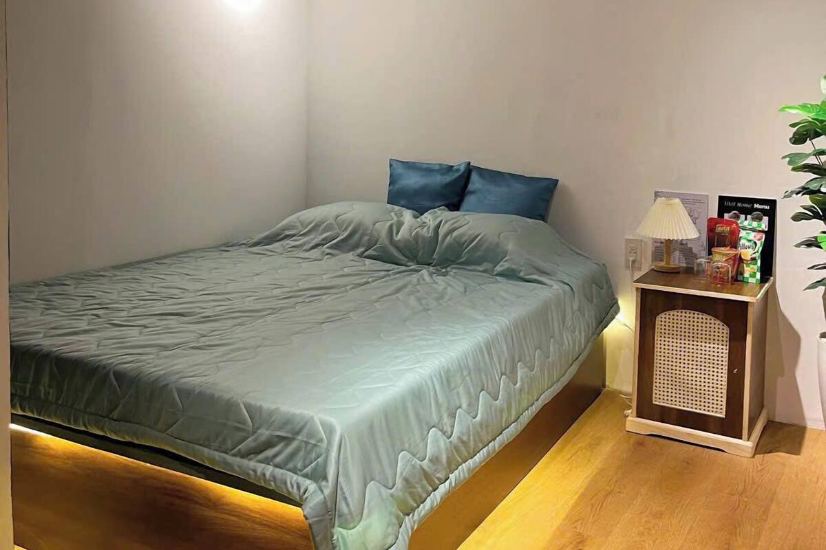 A bedroom with a bed, a bedside table, a lamp, and an air conditioning unit.