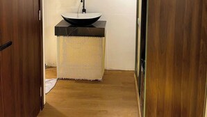 A bathroom with a wooden door, a round mirror, a black sink, and a large round mirror on the wall. - MMT Homestay (Can Tho)