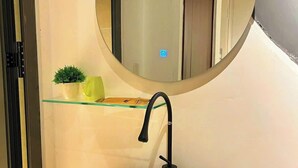 A modern bathroom with a round mirror, a white sink, and a small potted plant on a shelf. - MMT Homestay (Can Tho)