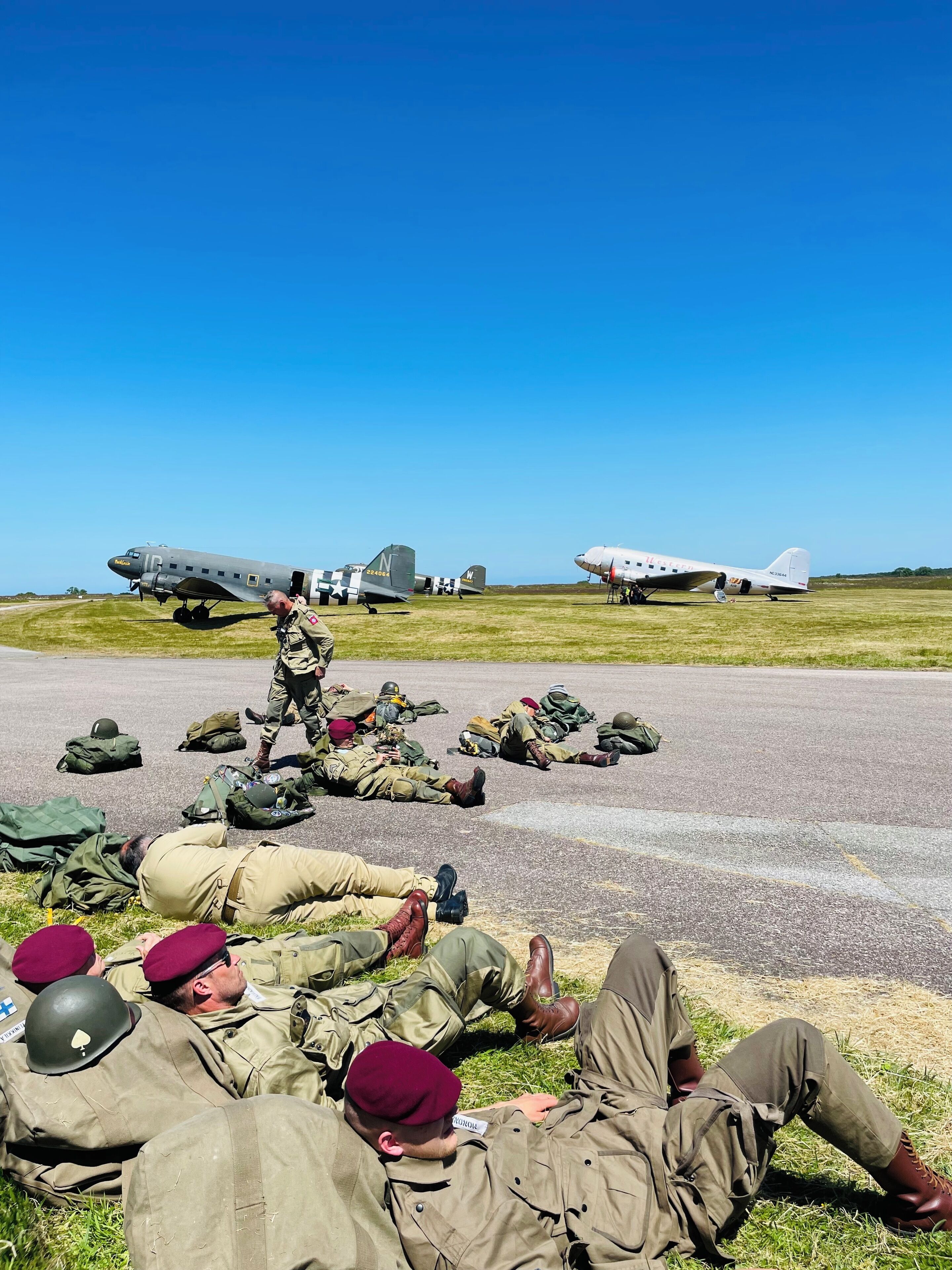 A group of people in military uniforms lying on the ground, with two airplanes in the background.