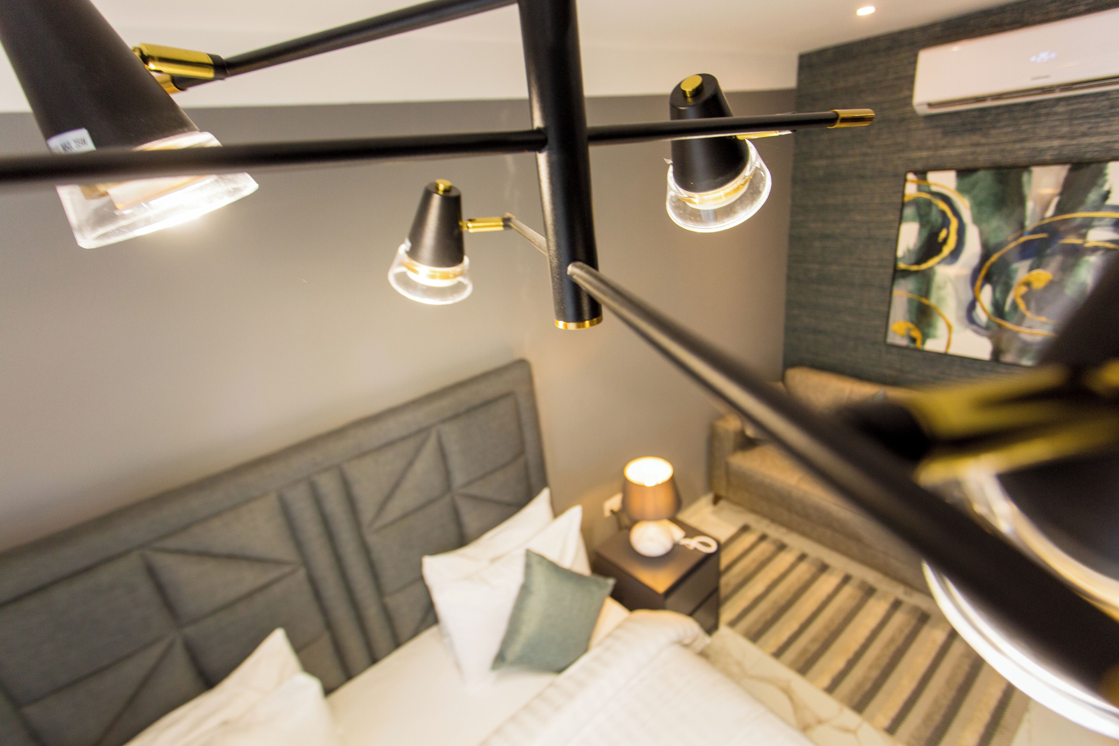 Hotellihuone, jossa on sänky, yöpöytä, lamppu ja taulu seinällä.