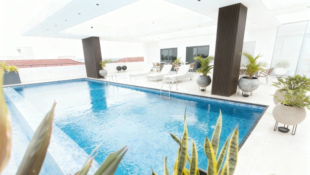 Un espace piscine intérieur moderne, avec une eau d’un bleu limpide, des chaises longues et des plantes en pot.