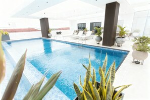 Un área de piscina interior moderna con agua azul cristalina, sillones de descanso y plantas en macetas.