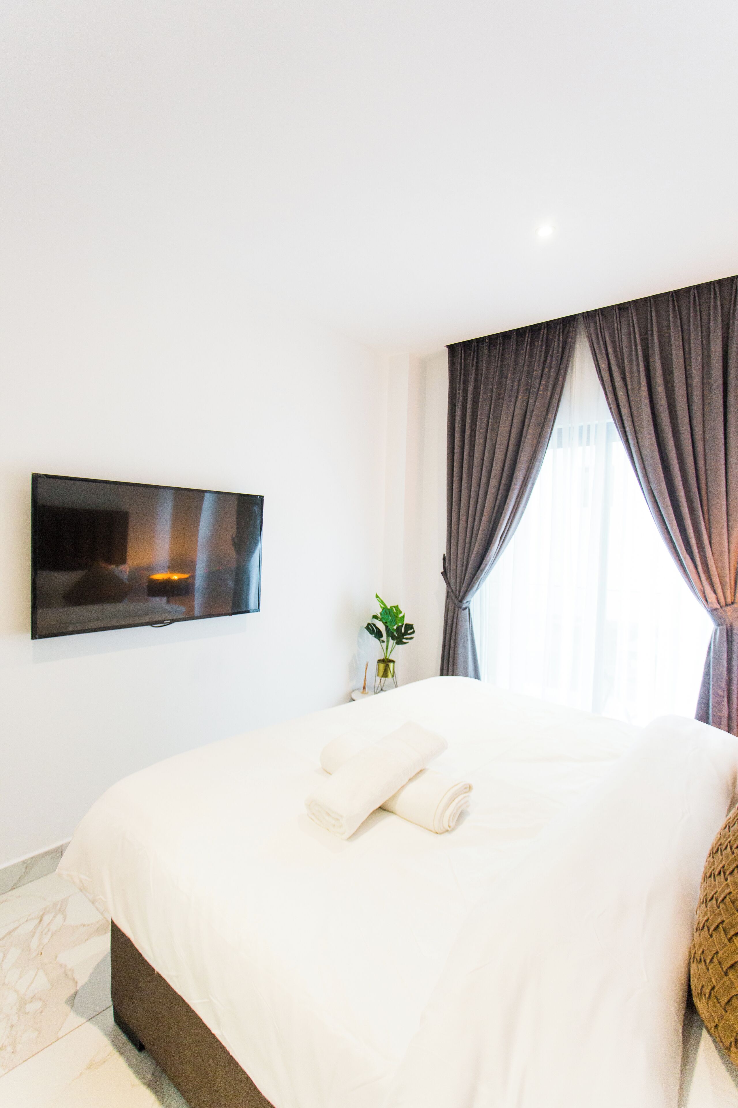 Ein modernes Hotelzimmer mit einem großen Bett, einem flachbildfernseher an der Wand und einem fenster mit Vorhängen.