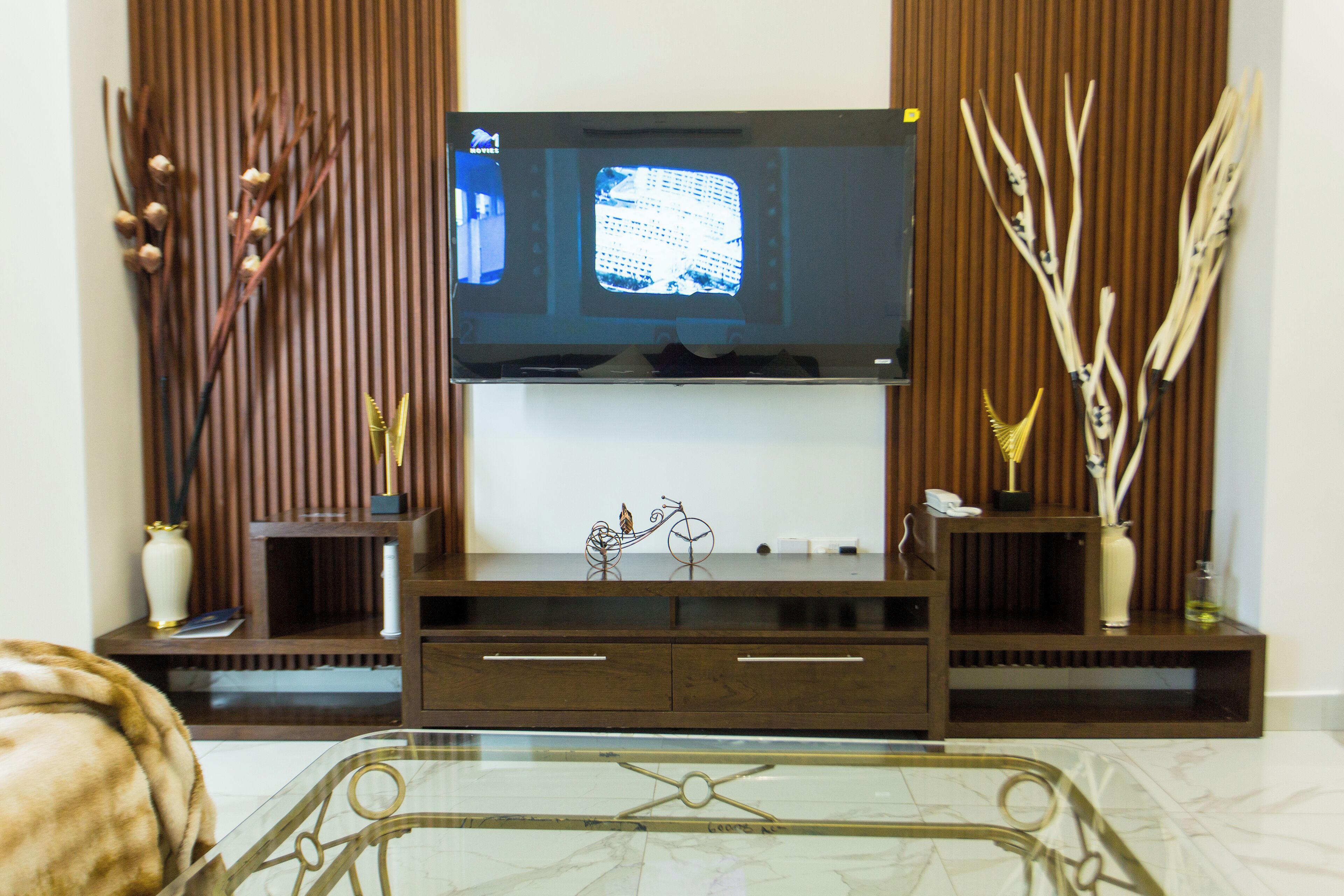 A living room with a flat-screen TV mounted on a wooden entertainment unit, flanked by decorative vases and branches.