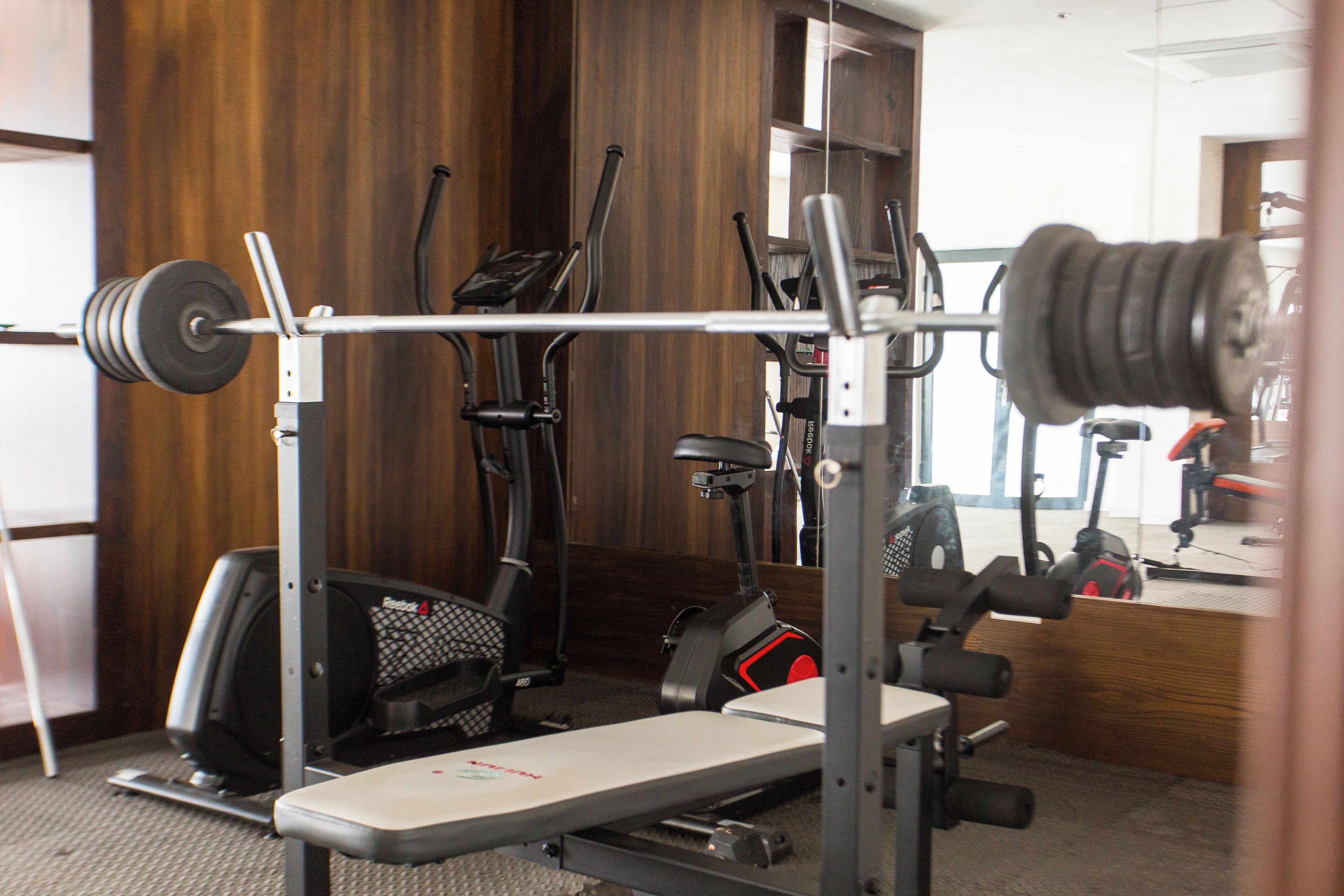 Une salle de sport équipée d’un banc de développé couché, d’un support à squats et de divers appareils de cardio.