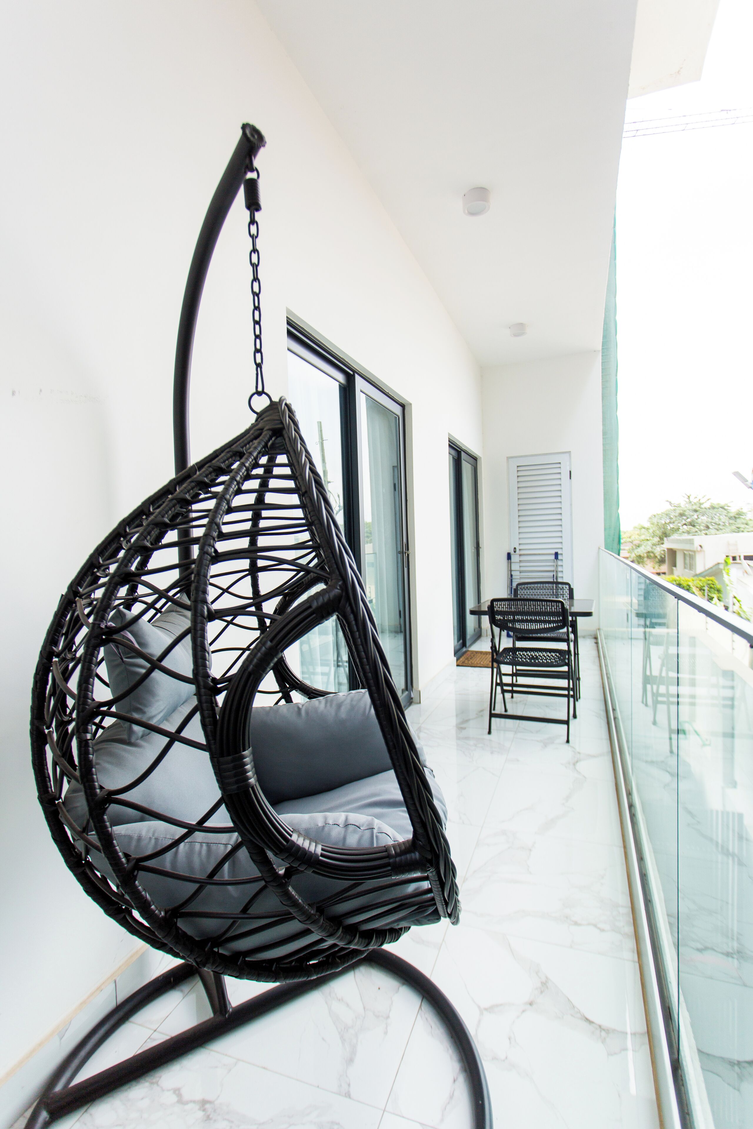 A balcony with a hanging chair, a table, and a chair.