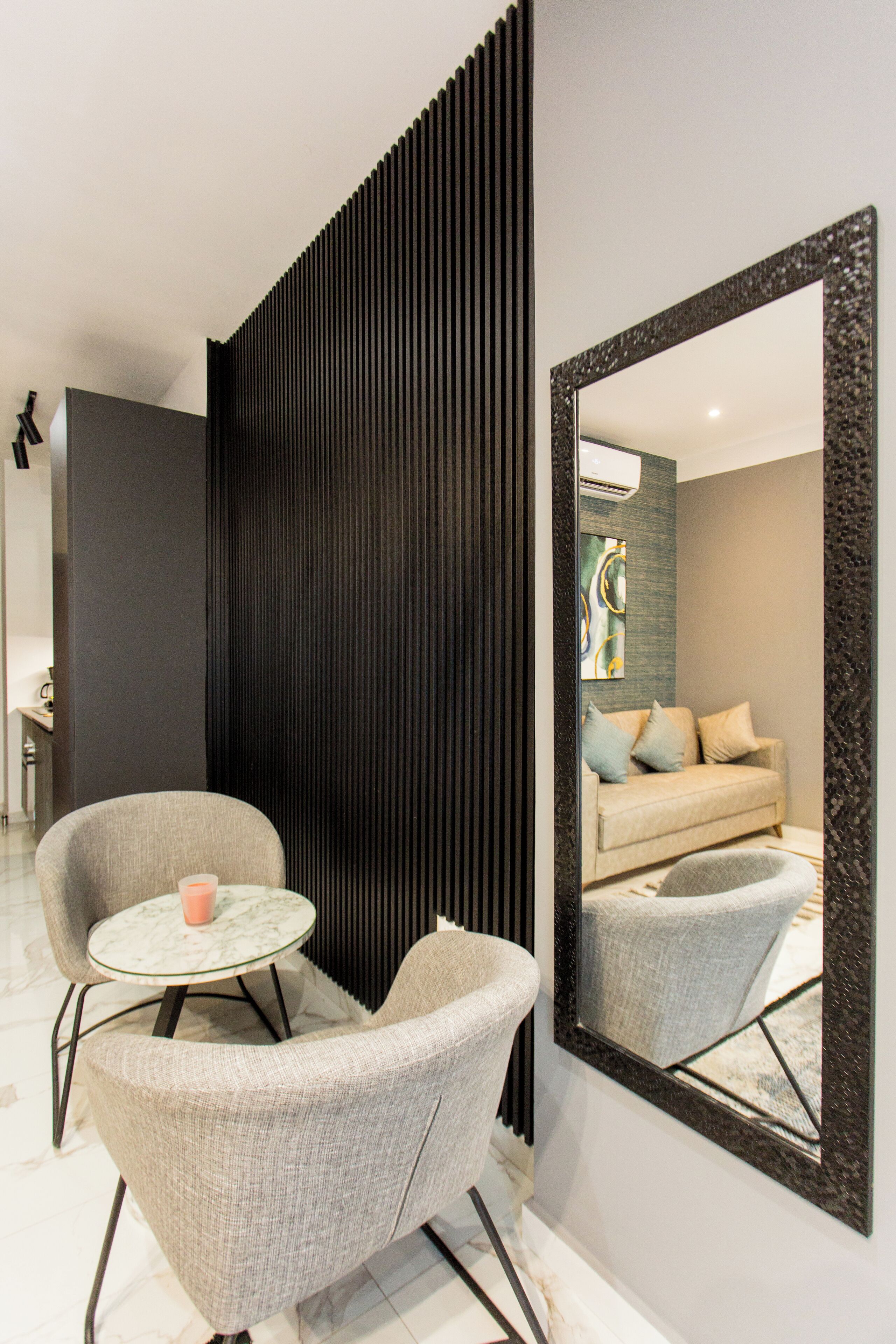 A modern living room with a sofa, two armchairs, a coffee table, and a large mirror.