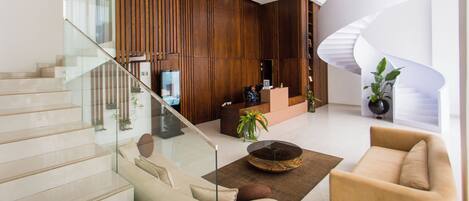 A modern lobby with a glass staircase, wooden paneling, a reception desk, and a spiral staircase.