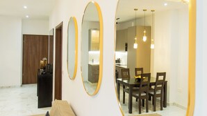 Un salon moderne avec un canapé beige, trois miroirs fixés au mur et un coin repas comprenant une table et des chaises.