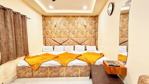 Un dormitorio con un cabecero estampado, una cama con ropa de cama blanca y una manta amarilla, una mesita de noche de madera con un reloj, y un espejo en la pared.