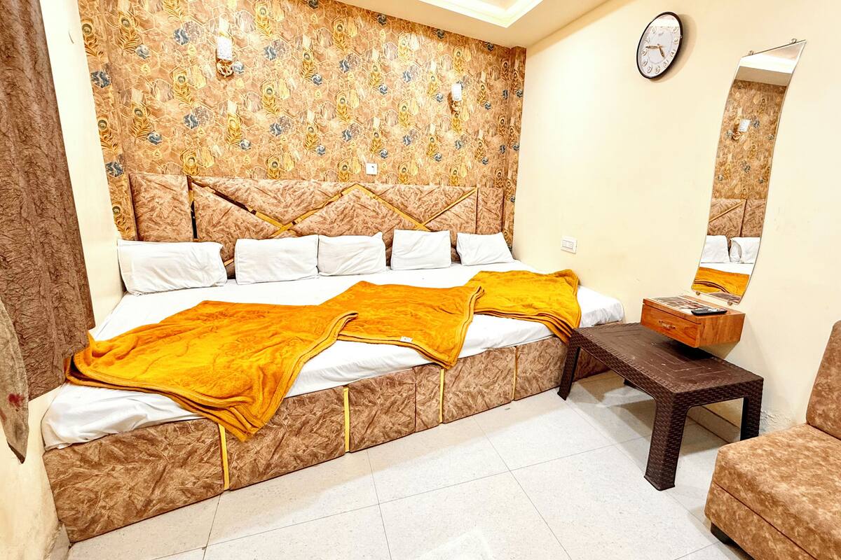 A bedroom with a patterned headboard, a bed with white and yellow bedding, a bedside table with a lamp, a chair, and a clock on the wall.