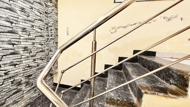 Una escalera con barandilla de metal, pared de piedra y pared beige con un ventanal pequeño.