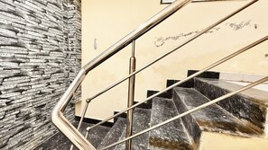 Un escalier avec une rampe métallique, un mur en pierre et un mur de couleur beige agrémenté d’une petite fenêtre.