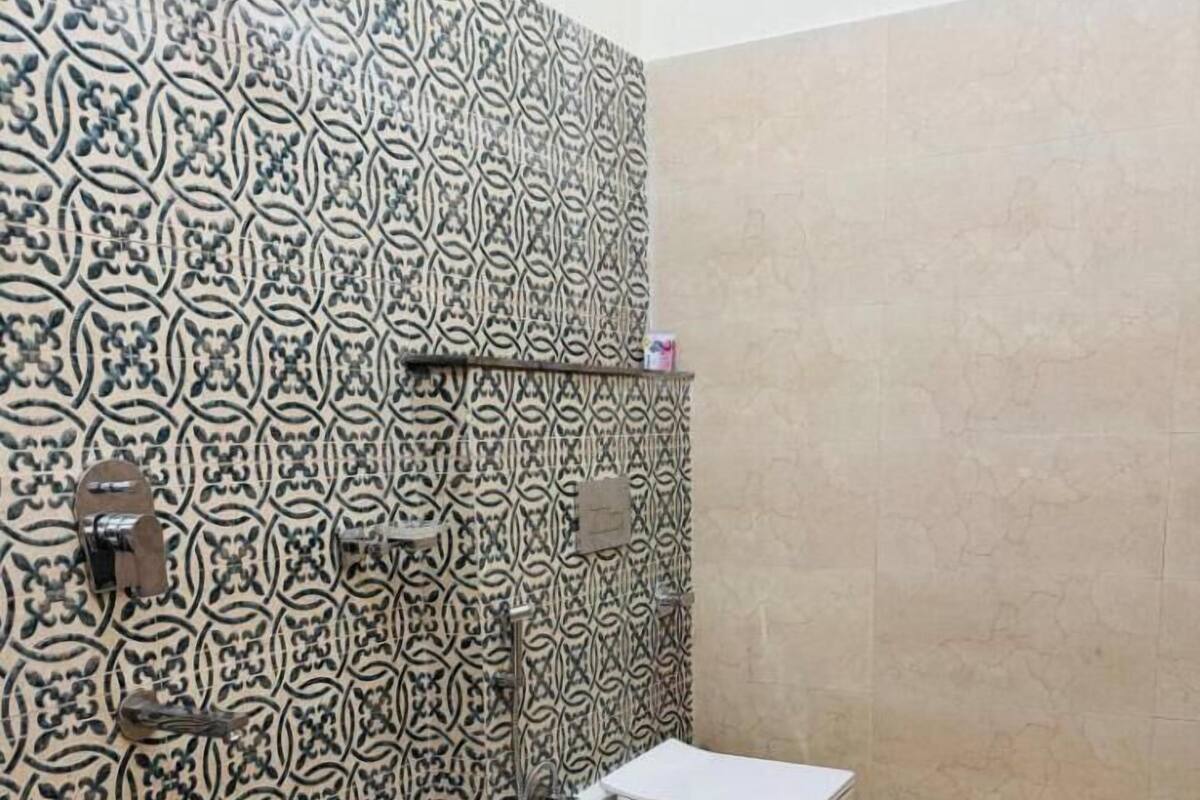 Casa de banho com azulejos estampados, sanita, um banquinho azul e um recipiente de plástico.