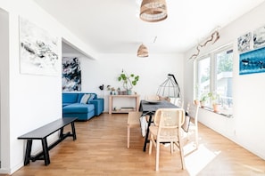 A modern living room with a blue sofa, dining table, wicker chairs, and artwork on the walls. - Spacious Family Home with Backyard (Stockholms län)