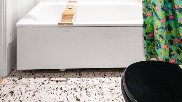 Une salle de bain avec une baignoire blanche, un rideau de douche à motifs tropicaux et un panier suspendu contenant des objets colorés.