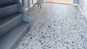 Una escalera con barandilla de metal que conduce a una habitación con piso moteado y vistas a un espacio exterior con una mesa de comedor.