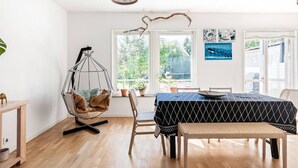 Una habitación con una silla colgante, una mesa de comedor con mantel estampado y vistas al exterior a través de grandes ventanales.