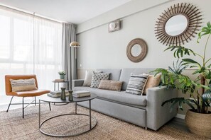 Ein modernes Wohnzimmer mit einem grauen Sofa, einem runden Couchtisch, einem braunen Ledersessel und zwei großen Spiegeln an der Wand.