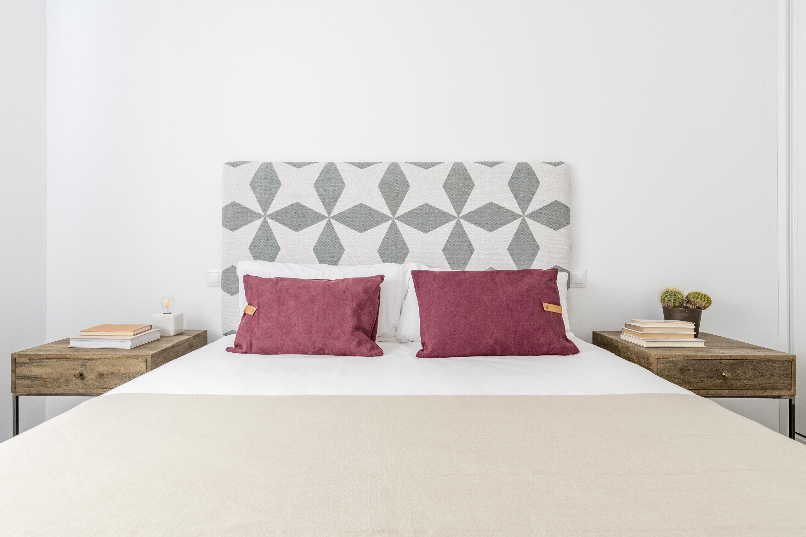 Ein Schlafzimmer mit einem Bett, zwei Nachttischen, einem Kopfteil mit geometrischem Muster und einer kleinen Topfpflanze auf einem Nachttisch.