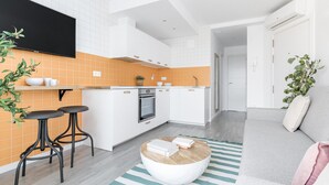 A modern kitchen with white cabinets, an orange backsplash, and a flat-screen TV mounted above the counter. - Cool Apartments by Olala Homes (Madrid)